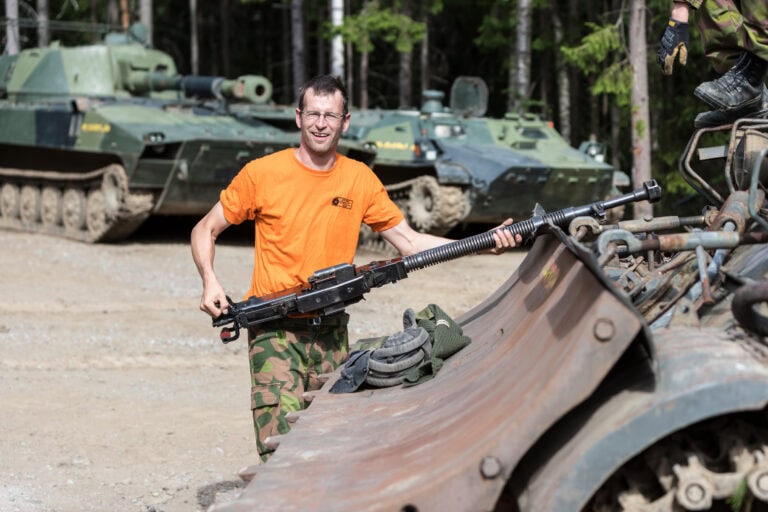 Mil-safarien Perustaja Mika Tanner hymyilee kantaessaan vaunun konekivääriä